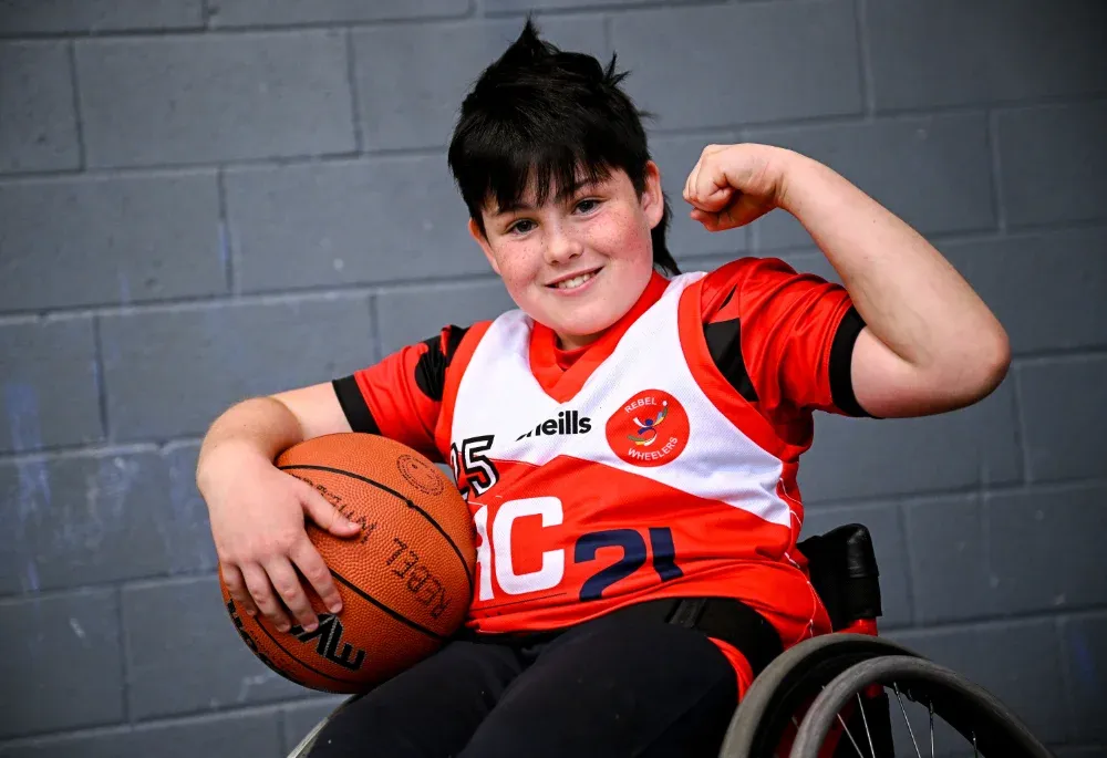 junior wheelchair basketball player holding a basketball and doing a bicep curl for the camera