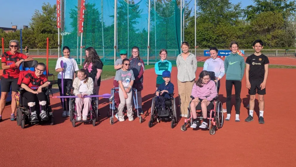 group of parents, volunteers and athletes in an athletics park posing for the camera